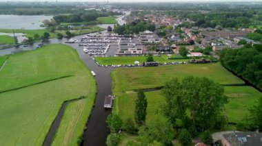 Ahşap rıhtımlar boyunca kenetlenmiş bir marina manzarası, yeşil parklar ve doğal otlaklarla çevrili dar bir su yolunda seyreden bir tekne..