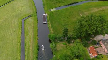Ahşap rıhtımlar boyunca kenetlenmiş bir marina manzarası, yeşil parklar ve doğal otlaklarla çevrili dar bir su yolunda seyreden bir tekne..