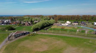 Modern binalar, ağaçlar ve yürüyüş yolları ile çevrili çimenlerle kaplı tarihi bir askeri kalenin havadan görünüşü, kıyı şeridi yakınlarında parlak mavi bir gökyüzünün altında..