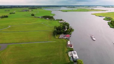 Yeşil tarlaların manzaralı manzarası, sakin bir nehir ve rahat göl evleri. Huzurlu kırsal alanlar ve uzak tarım arazileriyle çevrili bir tur teknesi suda süzülüyor..