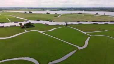 Bereketli yeşil tarlalar boyunca uzanan dar bir kanalın havadan görünüşü ve berrak mavi gökyüzünün altında limanı ve demirlemiş yatları olan huzurlu bir Hollanda köyüne uzanan küçük bir orman. Güzel bir rüzgar değirmeni.