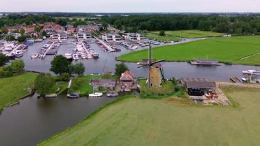 Kanal boyunca beyaz yelkenli bir yat. Güzel bir yel değirmeni. Dar bir kanalın havadan görünüşü yemyeşil çayırlarda akıyor ve küçük bir orman huzur dolu bir marinayla Hollanda köyüne gidiyor.