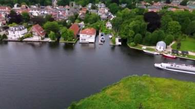 Yat ve rıhtımlarla dolu, yeşil çimenlikler ve şık deniz manzaralı evlerle çevrili modern bir marinadan bir tekne geçiyor. Sakin ve bulutlu bir günde yukarıdan sakin bir sahne çekiliyor..