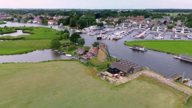 Kanal boyunca beyaz yelkenli bir yat. Güzel bir yel değirmeni. Dar bir kanalın havadan görünüşü yemyeşil çayırlarda akıyor ve küçük bir orman huzur dolu bir marinayla Hollanda köyüne gidiyor.