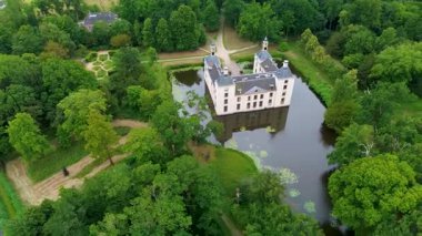 Uçsuz bucaksız yeşil tarlaları, dolambaçlı su yolları ve Hollanda 'nın düz kırsalında parçalı bulutlu bir gökyüzünün altında uzanan bir nehirle çevrili tarihi bir şatonun havadan görünüşü..