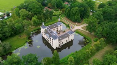 Uçsuz bucaksız yeşil tarlaları, dolambaçlı su yolları ve Hollanda 'nın düz kırsalında parçalı bulutlu bir gökyüzünün altında uzanan bir nehirle çevrili tarihi bir şatonun havadan görünüşü..