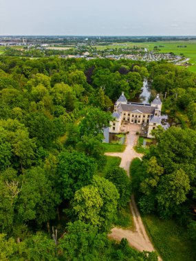 Uçsuz bucaksız yeşil tarlaları, dolambaçlı su yolları ve Hollanda 'nın düz kırsalında parçalı bulutlu bir gökyüzünün altında uzanan bir nehirle çevrili tarihi bir şatonun havadan görünüşü..
