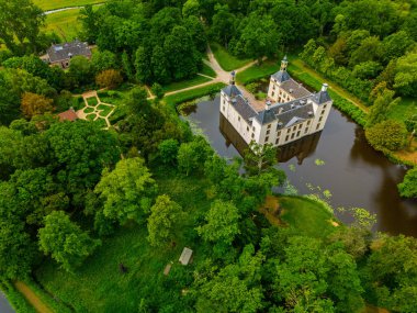 Uçsuz bucaksız yeşil tarlaları, dolambaçlı su yolları ve Hollanda 'nın düz kırsalında parçalı bulutlu bir gökyüzünün altında uzanan bir nehirle çevrili tarihi bir şatonun havadan görünüşü..