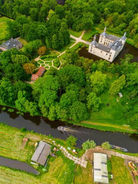 Uçsuz bucaksız yeşil tarlaları, dolambaçlı su yolları ve Hollanda 'nın düz kırsalında parçalı bulutlu bir gökyüzünün altında uzanan bir nehirle çevrili tarihi bir şatonun havadan görünüşü..
