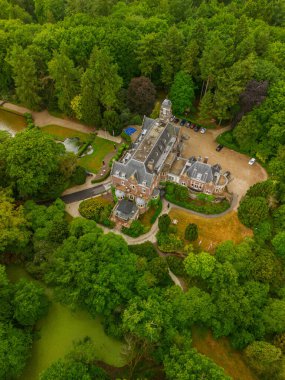 Etrafı yemyeşil ağaçlarla çevrili tarihi bir malikanenin havadan görünüşü ve çeşmesi, yürüyüş yolları ve park yeri olan güzel manzaralı bir bahçe. Sahne canlı yaz yeşilliklerini gösteriyor..