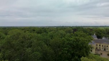 Uçsuz bucaksız yeşil tarlaları, dolambaçlı su yolları ve Hollanda 'nın düz kırsalında parçalı bulutlu bir gökyüzünün altında uzanan bir nehirle çevrili tarihi bir şatonun havadan görünüşü..