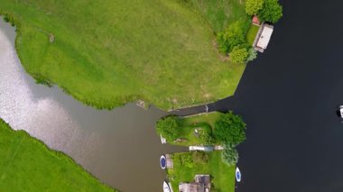 Dar bir kanalın havadan görünüşü yemyeşil çayırların arasından akıyor ve küçük bir orman huzurlu bir Hollanda köyüne götürüyor açık mavi gökyüzünün altında bir marinası ve demirlemiş yatları var..