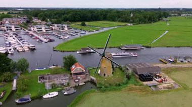 Kanal boyunca beyaz yelkenli bir yat. Güzel bir yel değirmeni. Dar bir kanalın havadan görünüşü yemyeşil çayırlarda akıyor ve küçük bir orman huzur dolu bir marinayla Hollanda köyüne gidiyor.