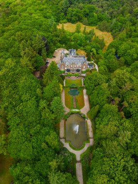 Etrafı yemyeşil ağaçlarla çevrili tarihi bir malikanenin havadan görünüşü ve çeşmesi, yürüyüş yolları ve park yeri olan güzel manzaralı bir bahçe. Sahne canlı yaz yeşilliklerini gösteriyor..