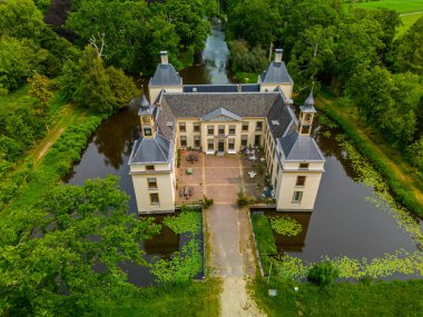 Uçsuz bucaksız yeşil tarlaları, dolambaçlı su yolları ve Hollanda 'nın düz kırsalında parçalı bulutlu bir gökyüzünün altında uzanan bir nehirle çevrili tarihi bir şatonun havadan görünüşü..