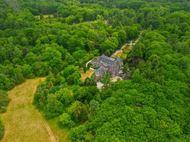 Etrafı yemyeşil ağaçlarla çevrili tarihi bir malikanenin havadan görünüşü ve çeşmesi, yürüyüş yolları ve park yeri olan güzel manzaralı bir bahçe. Sahne canlı yaz yeşilliklerini gösteriyor..