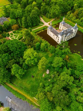 Uçsuz bucaksız yeşil tarlaları, dolambaçlı su yolları ve Hollanda 'nın düz kırsalında parçalı bulutlu bir gökyüzünün altında uzanan bir nehirle çevrili tarihi bir şatonun havadan görünüşü..