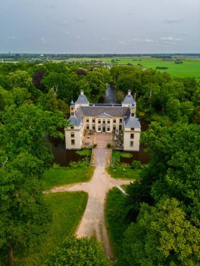 Uçsuz bucaksız yeşil tarlaları, dolambaçlı su yolları ve Hollanda 'nın düz kırsalında parçalı bulutlu bir gökyüzünün altında uzanan bir nehirle çevrili tarihi bir şatonun havadan görünüşü..