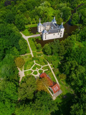 Uçsuz bucaksız yeşil tarlaları, dolambaçlı su yolları ve Hollanda 'nın düz kırsalında parçalı bulutlu bir gökyüzünün altında uzanan bir nehirle çevrili tarihi bir şatonun havadan görünüşü..