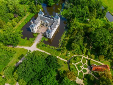 Uçsuz bucaksız yeşil tarlaları, dolambaçlı su yolları ve Hollanda 'nın düz kırsalında parçalı bulutlu bir gökyüzünün altında uzanan bir nehirle çevrili tarihi bir şatonun havadan görünüşü..