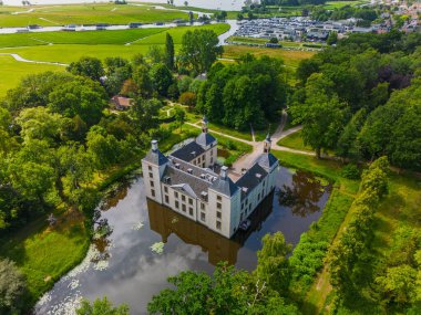 Uçsuz bucaksız yeşil tarlaları, dolambaçlı su yolları ve Hollanda 'nın düz kırsalında parçalı bulutlu bir gökyüzünün altında uzanan bir nehirle çevrili tarihi bir şatonun havadan görünüşü..