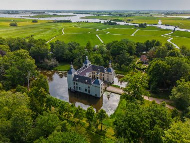 Uçsuz bucaksız yeşil tarlaları, dolambaçlı su yolları ve Hollanda 'nın düz kırsalında parçalı bulutlu bir gökyüzünün altında uzanan bir nehirle çevrili tarihi bir şatonun havadan görünüşü..