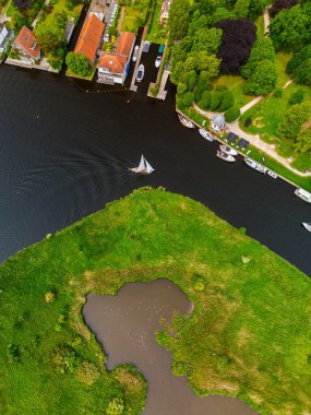 Suda süzülen evler, tekneler ve tek bir yelkenli sahnesi. Küçük bir göleti olan yemyeşil bir ada ve kuşlar manzaraya doğal bir güzellik katıyor..