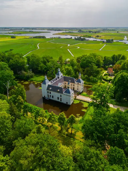 Uçsuz bucaksız yeşil tarlaları, dolambaçlı su yolları ve Hollanda 'nın düz kırsalında parçalı bulutlu bir gökyüzünün altında uzanan bir nehirle çevrili tarihi bir şatonun havadan görünüşü..