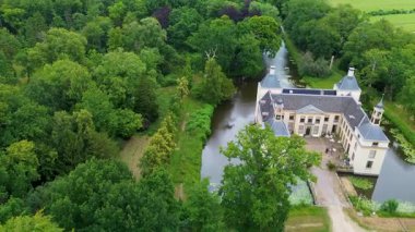 Uçsuz bucaksız yeşil tarlaları, dolambaçlı su yolları ve Hollanda 'nın düz kırsalında parçalı bulutlu bir gökyüzünün altında uzanan bir nehirle çevrili tarihi bir şatonun havadan görünüşü..