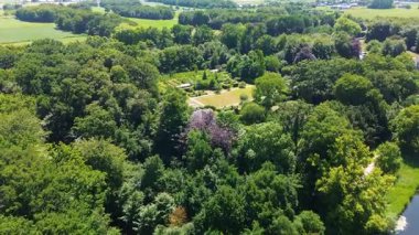 Yolları, yeşil çitleri ve sık ağaçlarla çevrili kırmızı çatılı binaları olan simetrik bir bahçenin havadan görünüşü. Huzurlu bir arazide doğa ve mimarinin mükemmel bir karışımı..