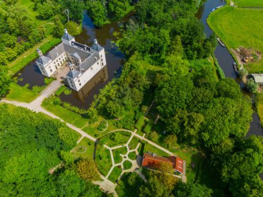 Uçsuz bucaksız yeşil tarlaları, dolambaçlı su yolları ve Hollanda 'nın düz kırsalında parçalı bulutlu bir gökyüzünün altında uzanan bir nehirle çevrili tarihi bir şatonun havadan görünüşü..