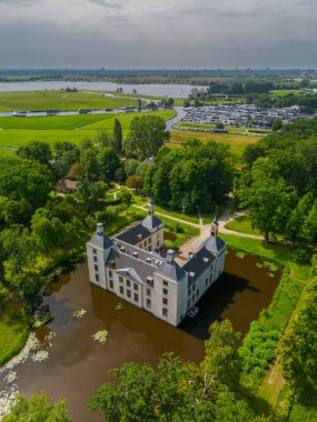 Uçsuz bucaksız yeşil tarlaları, dolambaçlı su yolları ve Hollanda 'nın düz kırsalında parçalı bulutlu bir gökyüzünün altında uzanan bir nehirle çevrili tarihi bir şatonun havadan görünüşü..