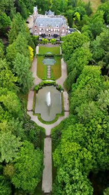 Etrafı yemyeşil ağaçlarla çevrili tarihi bir malikanenin havadan görünüşü ve çeşmesi, yürüyüş yolları ve park yeri olan güzel manzaralı bir bahçe. Sahne canlı yaz yeşilliklerini gösteriyor..