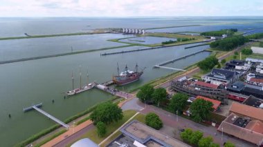 Liman, renkli binalar ve deniz boyunca kenetlenmiş sahte bir gemi olan bir sahil kasabasının havadan görüntüsü. Çevredeki alanlar arasında park alanları ve yeşil alanlar yer alıyor.