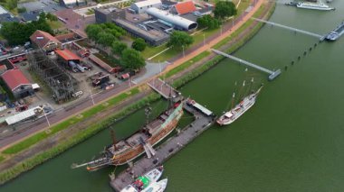 Liman, renkli binalar ve deniz boyunca kenetlenmiş sahte bir gemi olan bir sahil kasabasının havadan görüntüsü. Çevredeki alanlar arasında park alanları ve yeşil alanlar yer alıyor.