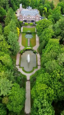 Etrafı yemyeşil ağaçlarla çevrili tarihi bir malikanenin havadan görünüşü ve çeşmesi, yürüyüş yolları ve park yeri olan güzel manzaralı bir bahçe. Sahne canlı yaz yeşilliklerini gösteriyor..