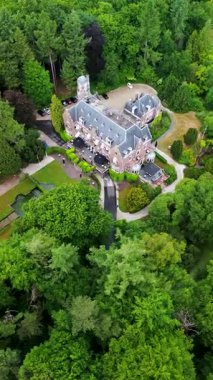 Etrafı yemyeşil ağaçlarla çevrili tarihi bir malikanenin havadan görünüşü ve çeşmesi, yürüyüş yolları ve park yeri olan güzel manzaralı bir bahçe. Sahne canlı yaz yeşilliklerini gösteriyor..