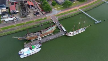 Lelystad, Flevoland, Hollanda - 09.06.2025: Limanı, renkli binaları ve su kenarı boyunca yanaşmış bir taklit gemisi olan kıyı kasabasının havadan görünüşü.