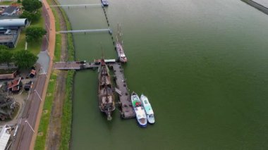 Lelystad, Flevoland, Hollanda - 09.06.2025: Limanı, renkli binaları ve su kenarı boyunca yanaşmış bir taklit gemisi olan kıyı kasabasının havadan görünüşü.