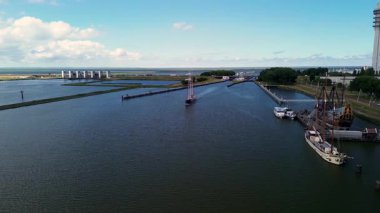 Lelystad, Flevoland, Hollanda - 09.06.2025: Parçalı bulutlu bir gökyüzü altında sakin sularda süzülen görkemli bir yelkenli gemi, kıyı manzaraları ve arka planda görünen modern bir baraj yapısı ile