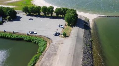 Dar bir barajın ya da dar bir geçidin havadan görünüşü her iki taraftaki geniş su kütleleri tarafından çevrelenmiş, dağınık bulutlarla dolu canlı mavi bir gökyüzünün altında ufka doğru yol alıyor..