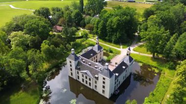 Uçsuz bucaksız yeşil tarlaları, dolambaçlı su yolları ve Hollanda 'nın düz kırsalında parçalı bulutlu bir gökyüzünün altında uzanan bir nehirle çevrili tarihi bir şatonun havadan görünüşü..