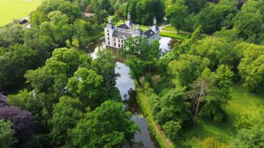 Uçsuz bucaksız yeşil tarlaları, dolambaçlı su yolları ve Hollanda 'nın düz kırsalında parçalı bulutlu bir gökyüzünün altında uzanan bir nehirle çevrili tarihi bir şatonun havadan görünüşü..