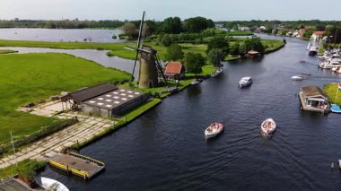 Kanal boyunca beyaz yelkenli bir yat. Güzel bir yel değirmeni. Dar bir kanalın havadan görünüşü yemyeşil çayırlarda akıyor ve küçük bir orman huzur dolu bir marinayla Hollanda köyüne gidiyor.