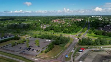 Liman, renkli binalar, uzun bir iletişim kulesi ve deniz kıyısına yanaşmış bir taklit gemi olan bir sahil kasabasının havadan görüntüsü. Çevredeki alanlar arasında park alanları ve yeşil alanlar yer alıyor.