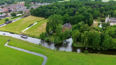 Yoğun bir ormanı, büyük tuğlalı bir evi ve yakınlardaki şatoya benzeyen bir binası olan huzurlu bir kırsal alan. Sakin kanalda dinlenen küçük tekneler ve arka planda sessiz bir köy var..