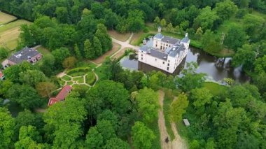 Uçsuz bucaksız yeşil tarlaları, dolambaçlı su yolları ve Hollanda 'nın düz kırsalında parçalı bulutlu bir gökyüzünün altında uzanan bir nehirle çevrili tarihi bir şatonun havadan görünüşü..