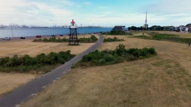 Sahil manzaralı sakin bir sahil kasabası kayalık bir kıyı şeridi, yeşil açık alanlar, geçen araçların olduğu bir yol ve açık mavi gökyüzünün altındaki konut binaları..