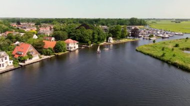 Ahşap rıhtımlar boyunca kenetlenmiş bir marina manzarası, yeşil parklar ve doğal otlaklarla çevrili dar bir su yolunda seyreden bir tekne..