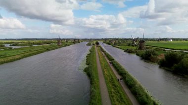 Yürüme yolları olan bir kanal kasabası, kıyı boyunca kenetlenmiş tekneler, yeşil alanlar ve bulutlu gökyüzü. Doğanın ve küçük kasaba hayatının karışımıyla huzurlu bir nehir kenarı manzarası..
